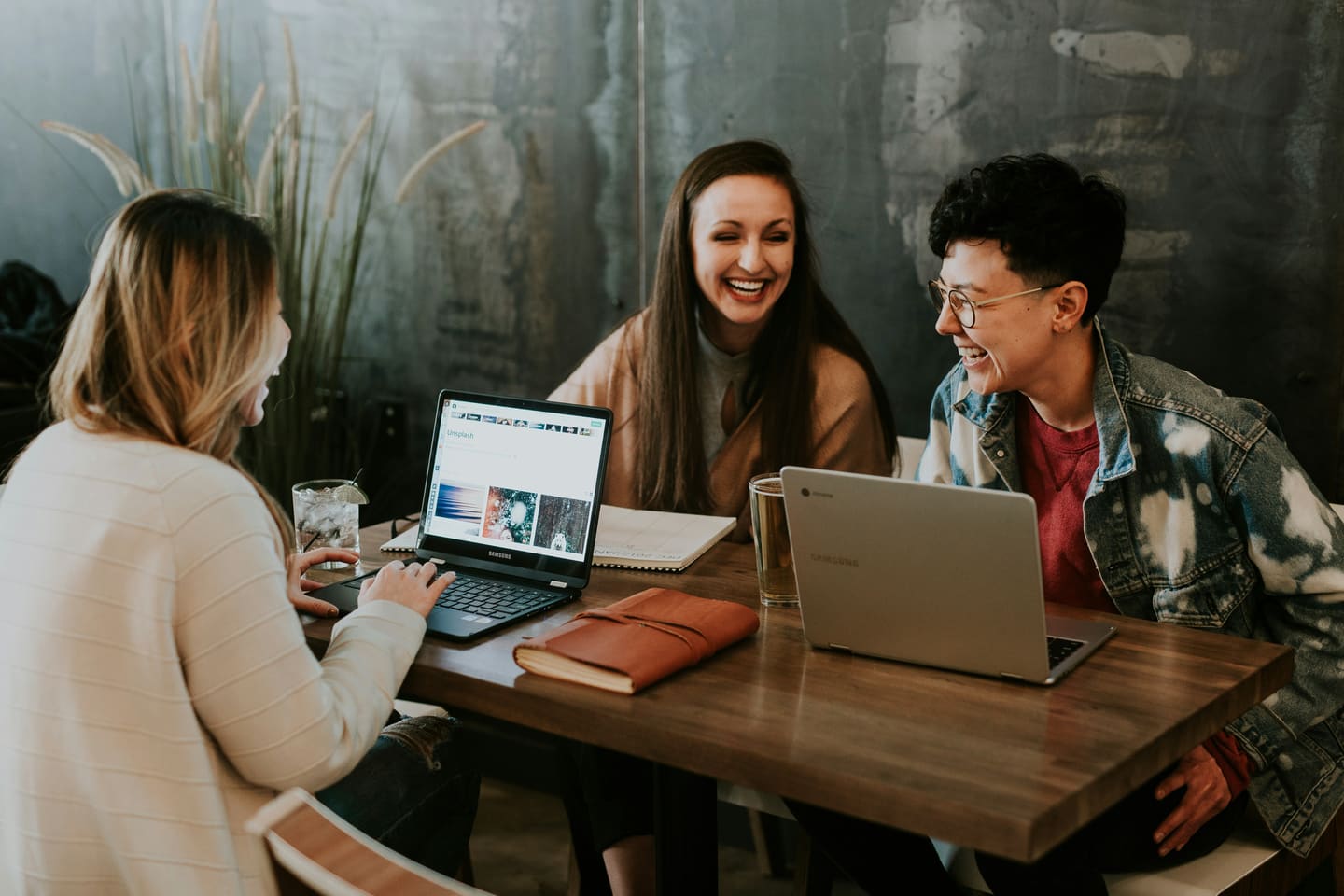 Three colleagues laughing together around a table with laptops.